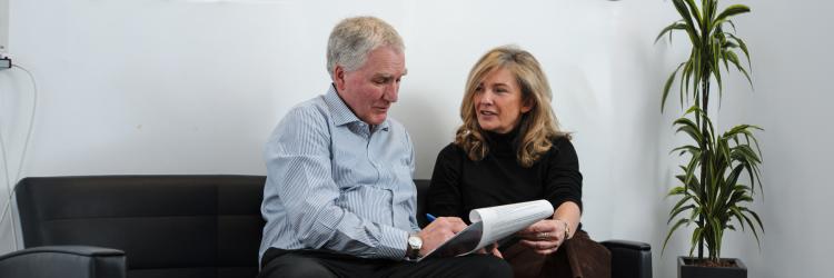 A couple are sat in a clinic waiting room, looking at medical documents