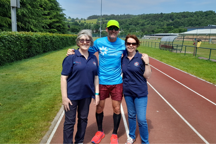 Very hot day at Stirling University's running track. Pictured left to right are Kerry Mackay, Gregor Miller and Pam Macdonald. Gregor is wearing a Euan MacDonald Centre running shirt and Kerry and Pam are wearing Euan MacDonald Centre polo shirts. Pam and Kerry have walked 10 laps, Gregor is attempting to run 100 miles. Everyone is smiling in the picture with a clear blue Scottish summer sky.