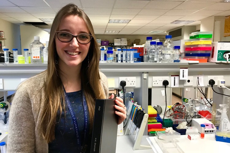Hannah Shorrock in the lab holding a copy of her PhD thesis