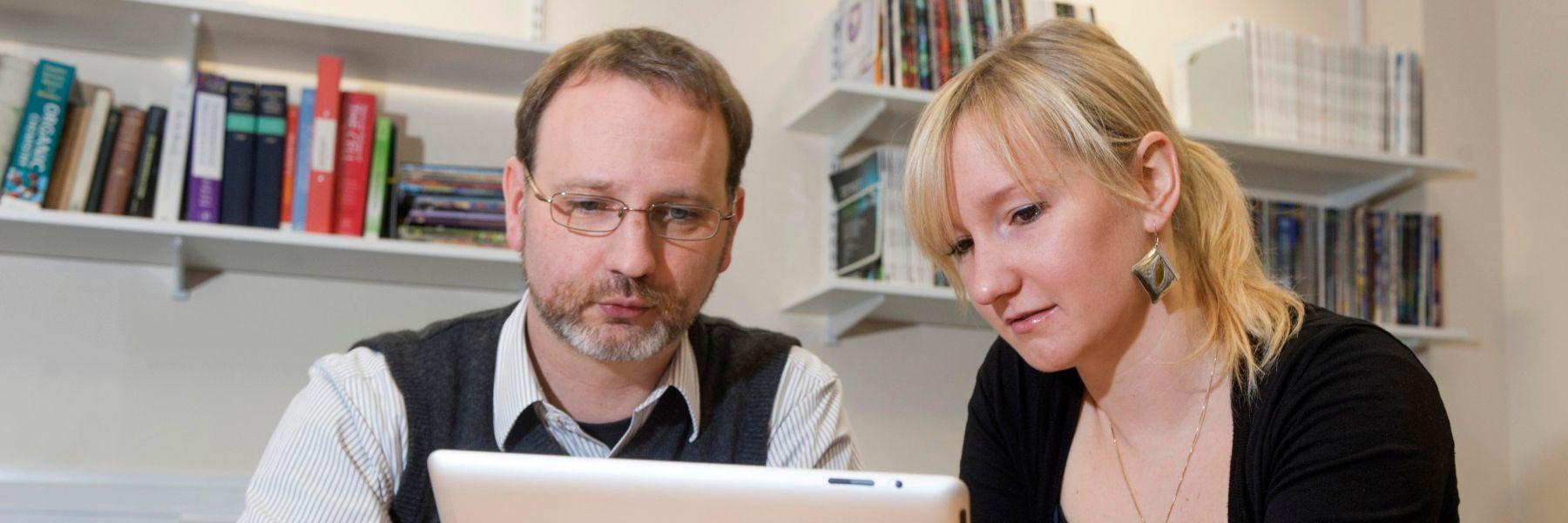 Two people in relaxed discussion looking at an iPad